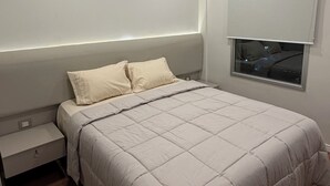 A bedroom with a bed, bedside table, and a window.