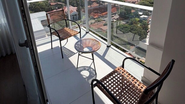 A balcony with two chairs and a small table, overlooking a cityscape with various buildings.