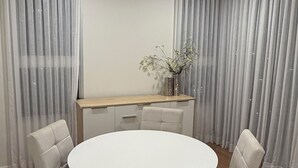 A modern dining room with a round table and four chairs, a wooden desk, and a vase with flowers.