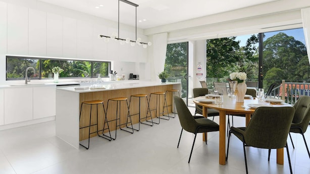 A modern kitchen with a large island, bar stools, and a dining area with a round table and chairs.