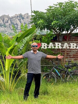 A person standing in front of a sign that reads "BARAB" with a brick wall and greenery in the background.