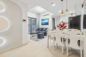 A modern living room with a grey sofa, a dining table with white chairs, and a kitchen area with a black refrigerator. - MASTERI Premier Residence (Thao Dien)