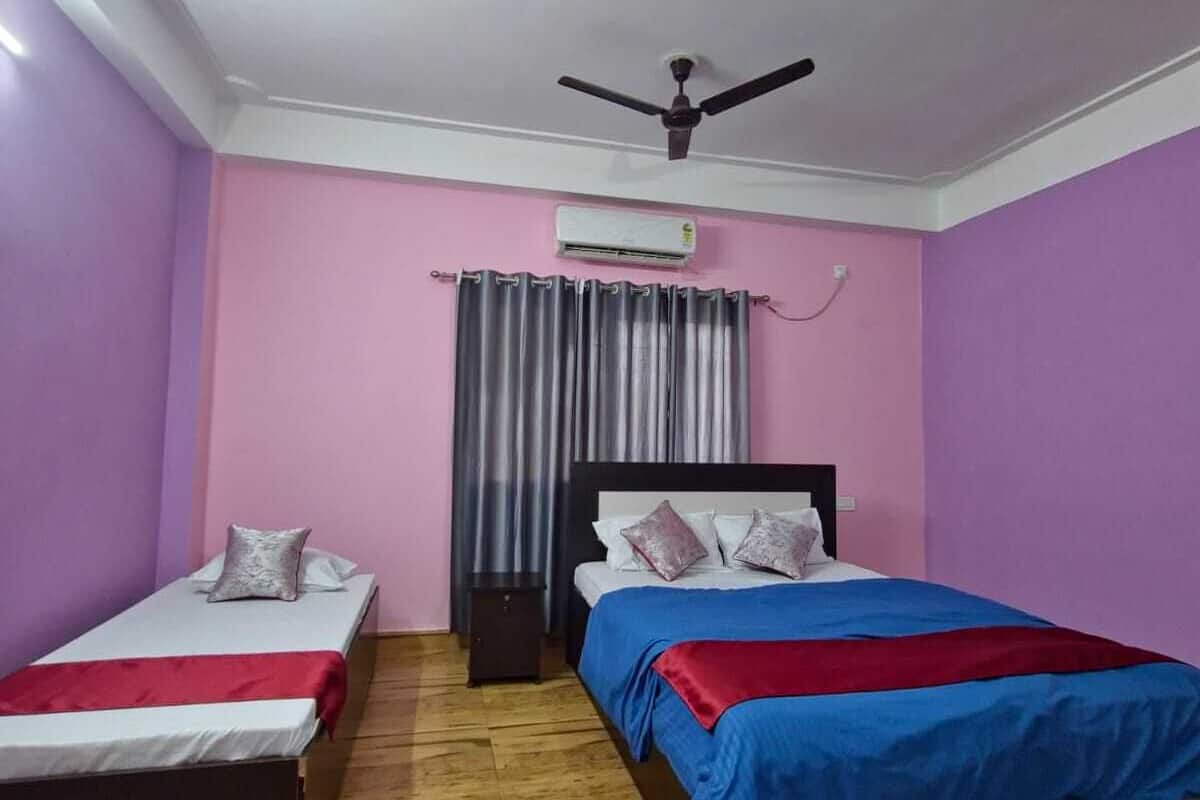 A bedroom with two single beds and one double bed, a ceiling fan, an air conditioning unit, and a window with curtains.
