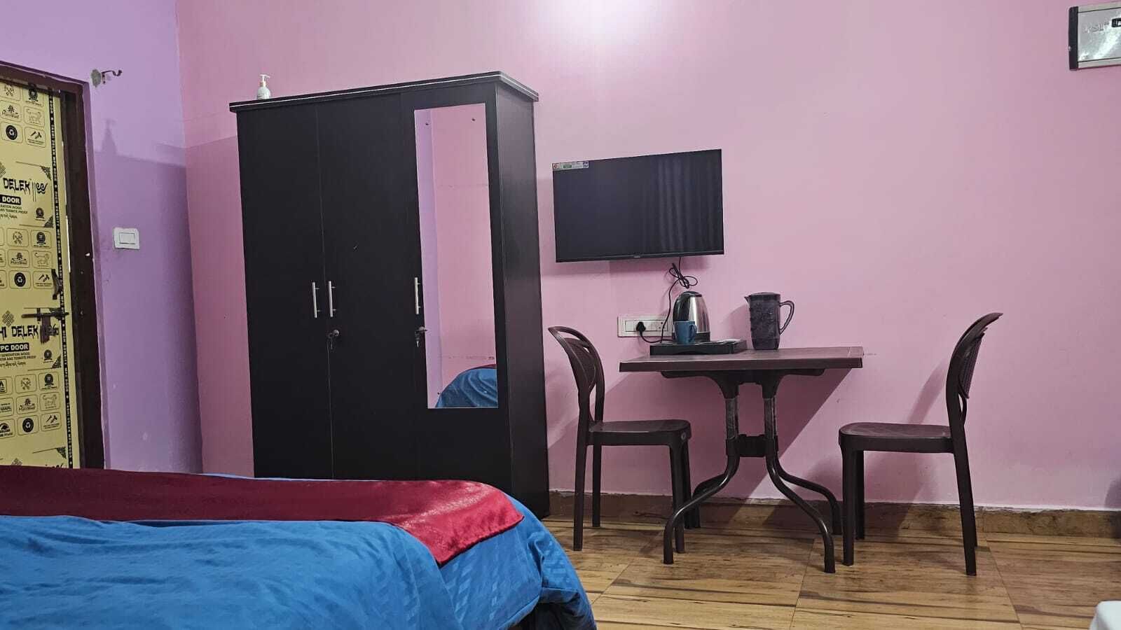A bedroom with a bed, a wardrobe, a desk with a chair, a television, and a wall-mounted shelf.