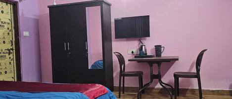 A bedroom with a bed, a wardrobe, a desk with a chair, a television, and a wall-mounted shelf.