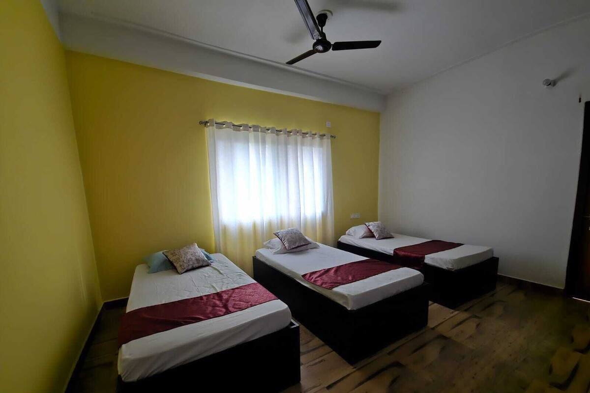 A room with three beds arranged in a row, a ceiling fan, and a window with curtains.