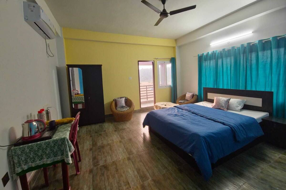 A hotel room with a bed, a table with a chair, a wardrobe, a ceiling fan, and a window with curtains.