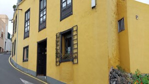 A yellow building with black shutters, a door, and a small window with plants. - English-Style Apartment only for Adults (Icod de los Vinos, Tenerife)