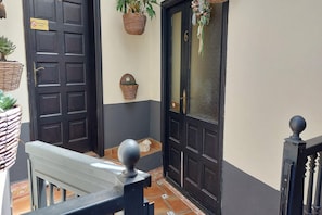 A black door with a sign, a potted plant, and a small shelf with a decorative item.