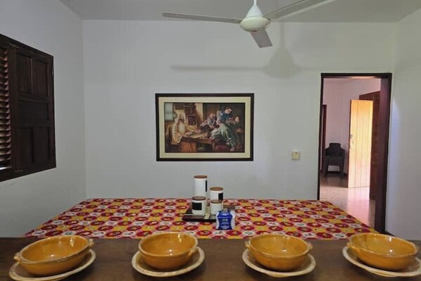 A dining area with a table set for four, a ceiling fan, and a framed painting on the wall.