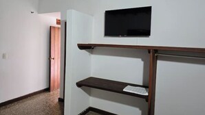 Un couloir avec une porte en bois, un téléviseur fixé au mur et une étagère.