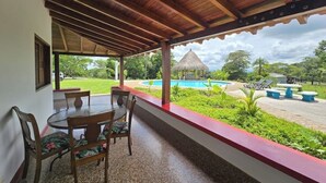 En overdækket terrasse med pool, stole og udsigt over poolområdet.