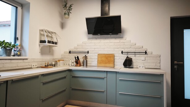 A modern kitchen with a white brick backsplash, green cabinets, a wooden cutting board, and a hanging pot rack. - Stylish time-out near Nuremberg/Herzogenaurach (Hagenbüchach)
