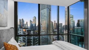 A modern hotel room with a large window offering a city skyline view. - Stunning 2-bed Apartment With City Views (Melbourne)