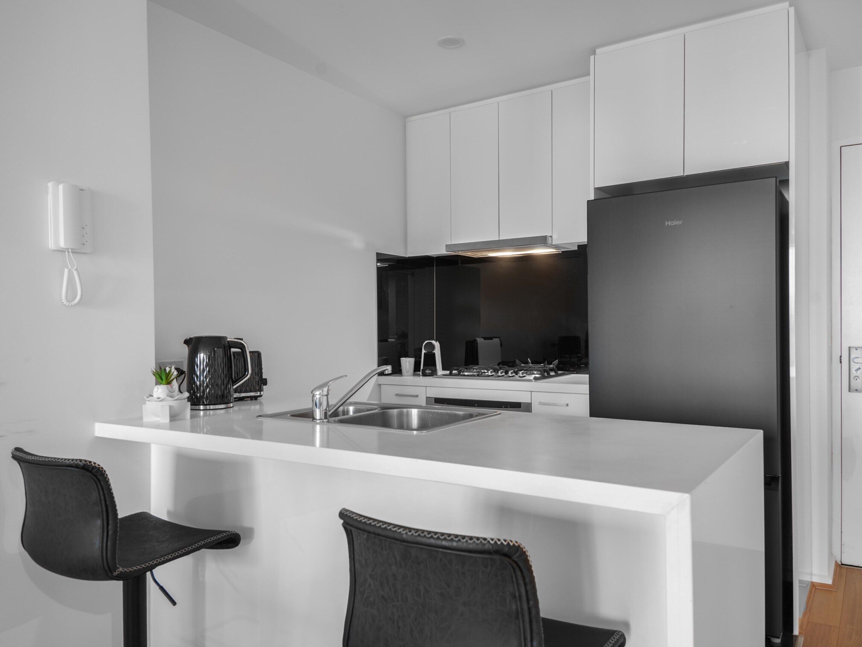 A modern kitchen with white cabinets, a black refrigerator, and a coffee maker on the counter.