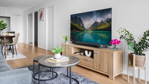 A modern living room with a flat-screen TV, wooden cabinet, and a dining area with chairs and a table. - Stunning 2-bed Apartment With City Views (Melbourne)