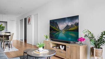 A modern living room with a flat-screen TV, wooden cabinet, and a dining area with chairs and a table.