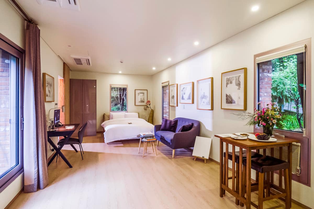A hotel room with a bed, a desk, a sofa, a dining table, and framed pictures on the walls.