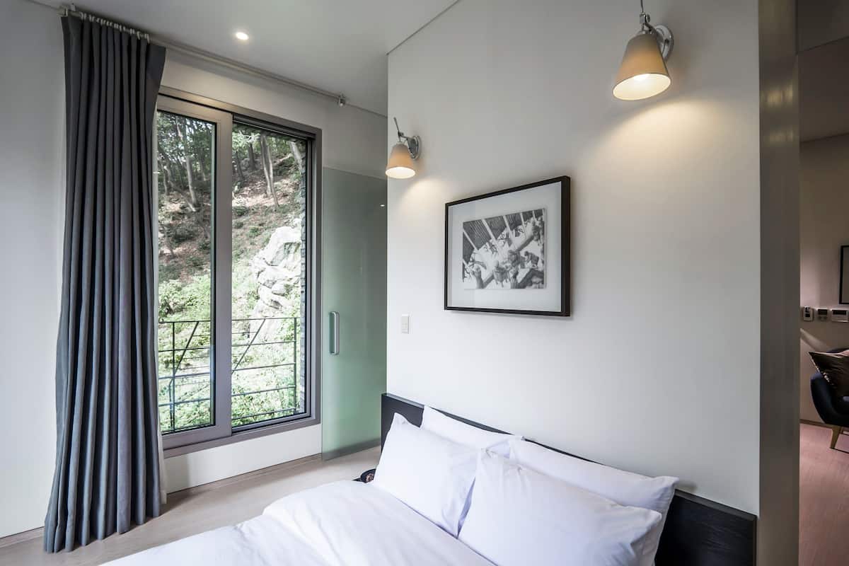 A modern hotel room with a large bed, a framed picture on the wall, and a window with curtains.