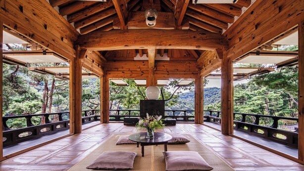 A wooden pavilion with a central table and cushions, surrounded by a railing with a view of a forested hillside. - L'art de la vie Art & Resorts (Icheon)