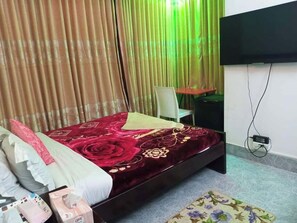 A bedroom with a bed, a chair, a small table, a TV, and a power outlet. - Hotel Raiyan Int Jamalpur (Jamalpur)