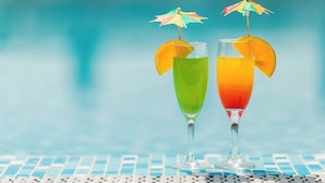 Dos cócteles con sombrillas en una mesa junto a la piscina.