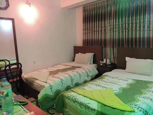 A hotel room with two beds, a nightstand, a chair, a table with a water bottle, and a window with curtains. - Hotel Raiyan Int Jamalpur (Jamalpur)