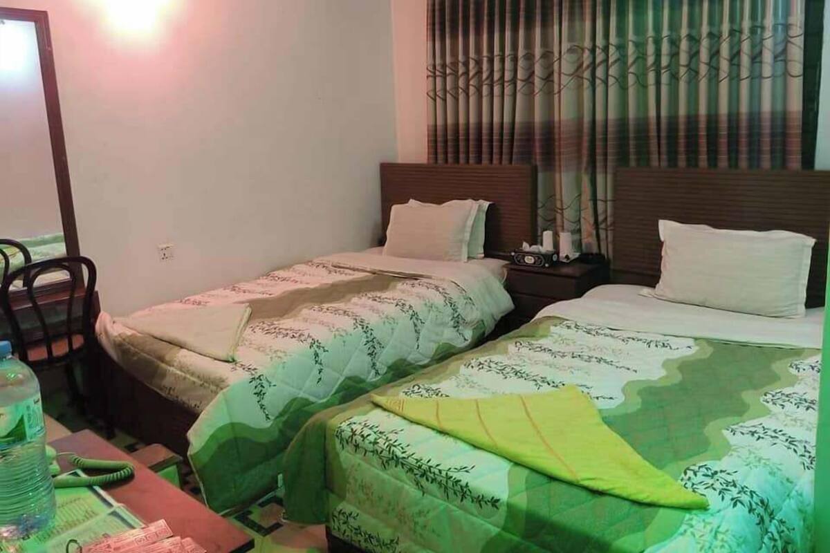 A hotel room with two single beds, a nightstand, a chair, and a table with a water bottle.