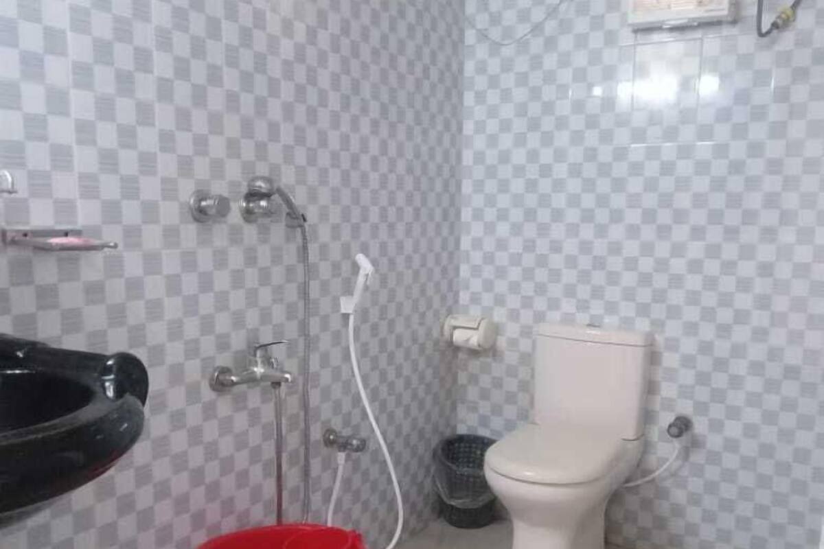 A bathroom with a checkered tile wall, a white toilet, a black sink, and a red bucket.