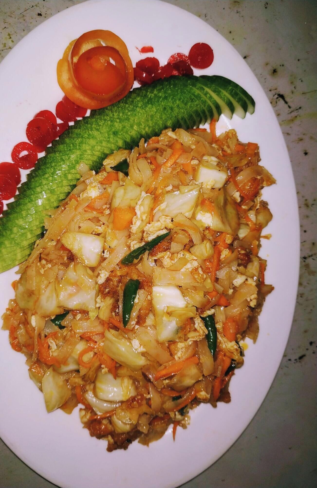 A plate of food with vegetables and eggs, garnished with a cucumber and tomato slice.
