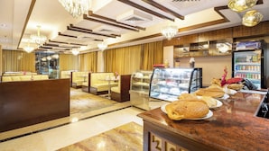 Un hall de hotel con áreas de descanso, una vitrina con pasteles y un refrigerador lleno de bebidas.