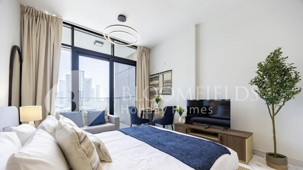 Habitación de hotel moderna con una cama grande, televisor y vistas a la ciudad a través de amplios ventanales.