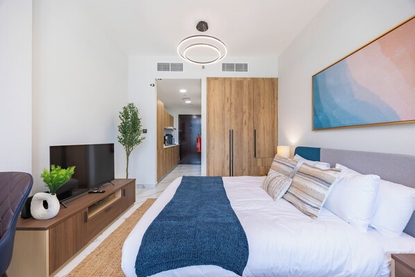 Habitación de hotel moderna con cama, televisor, planta y un cuadro en la pared.