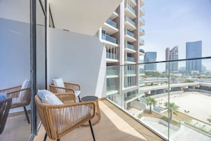 Un balcón con mobiliario de mimbre, baranda de vidrio y vistas a una ciudad moderna y la playa.