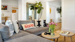 En moderne stue med en grå sofa, dekorative puder, en vase med blomster og et rundt træbord.