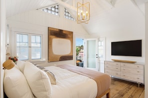 Ein Schlafzimmer mit einem großen Bett, einem Schminktisch, einem Fernseher und Blick nach draußen.
