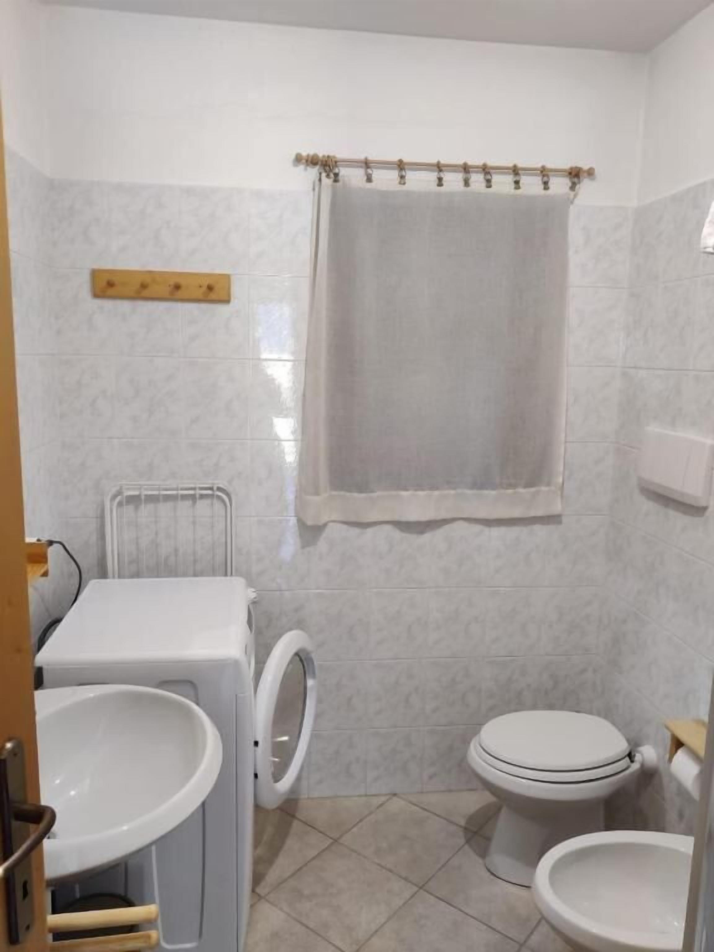 A small, compact bathroom with a washing machine, two toilets, and a shower curtain.