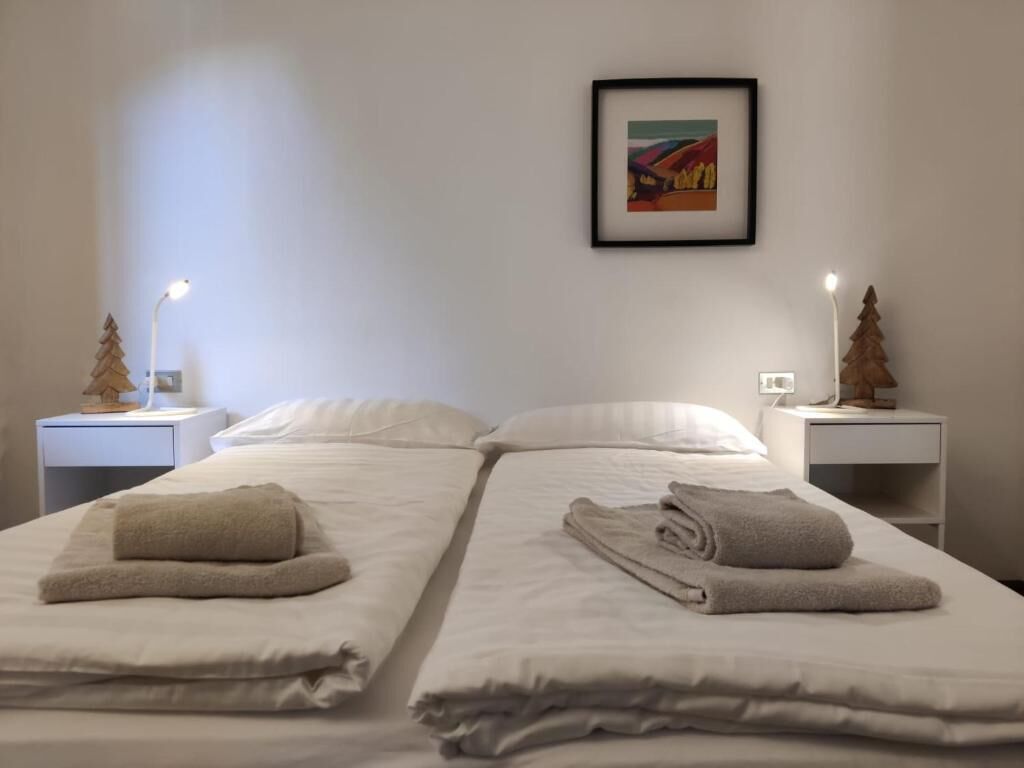 A hotel room with two beds, each with a neatly folded towel and a small wooden tree on the nightstand.