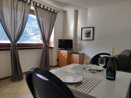 Un coin repas avec une table dressée pour deux personnes, une bouteille de vin Zonin et un téléviseur en arrière-plan.