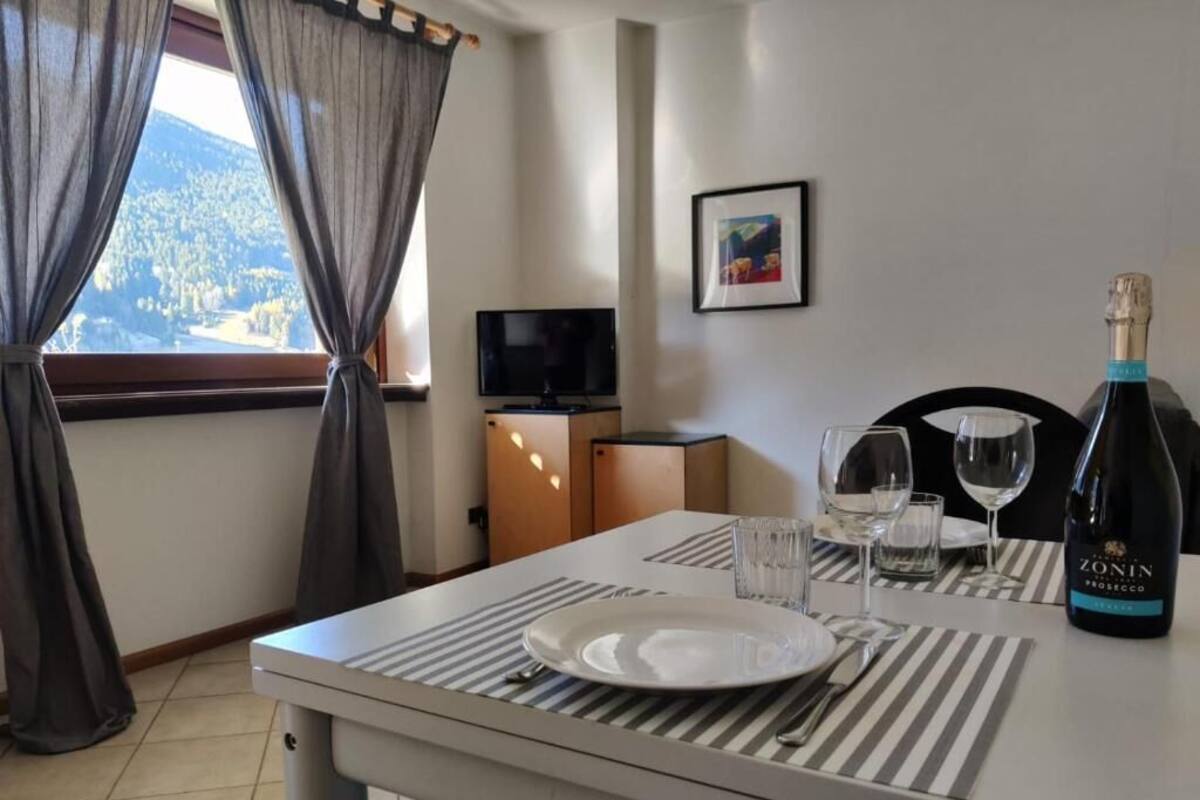 A dining area with a table set for two, a bottle of Zonin Prosecco, and a television in the background.