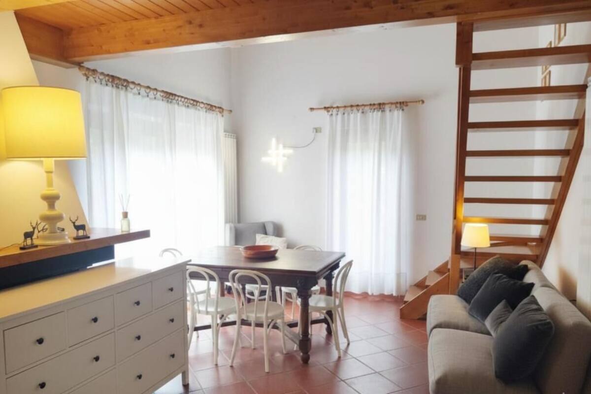 A dining area with a wooden table and chairs, a sofa, a staircase, and a lamp.