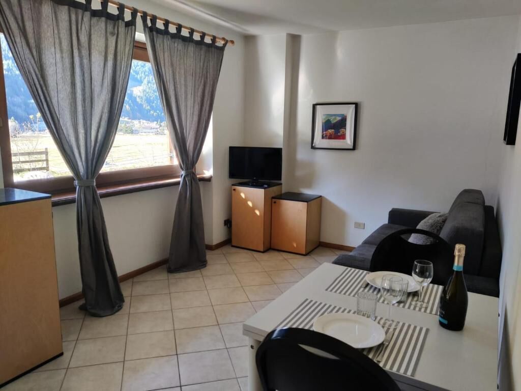 A modern living room with a sofa, a dining table set for two, a TV, and a window with curtains.