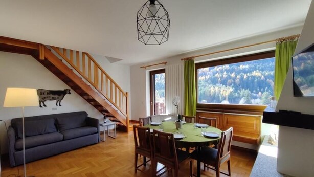 Et spiseområde med et træbord og stole, en sofa, en lampe og en trappe.