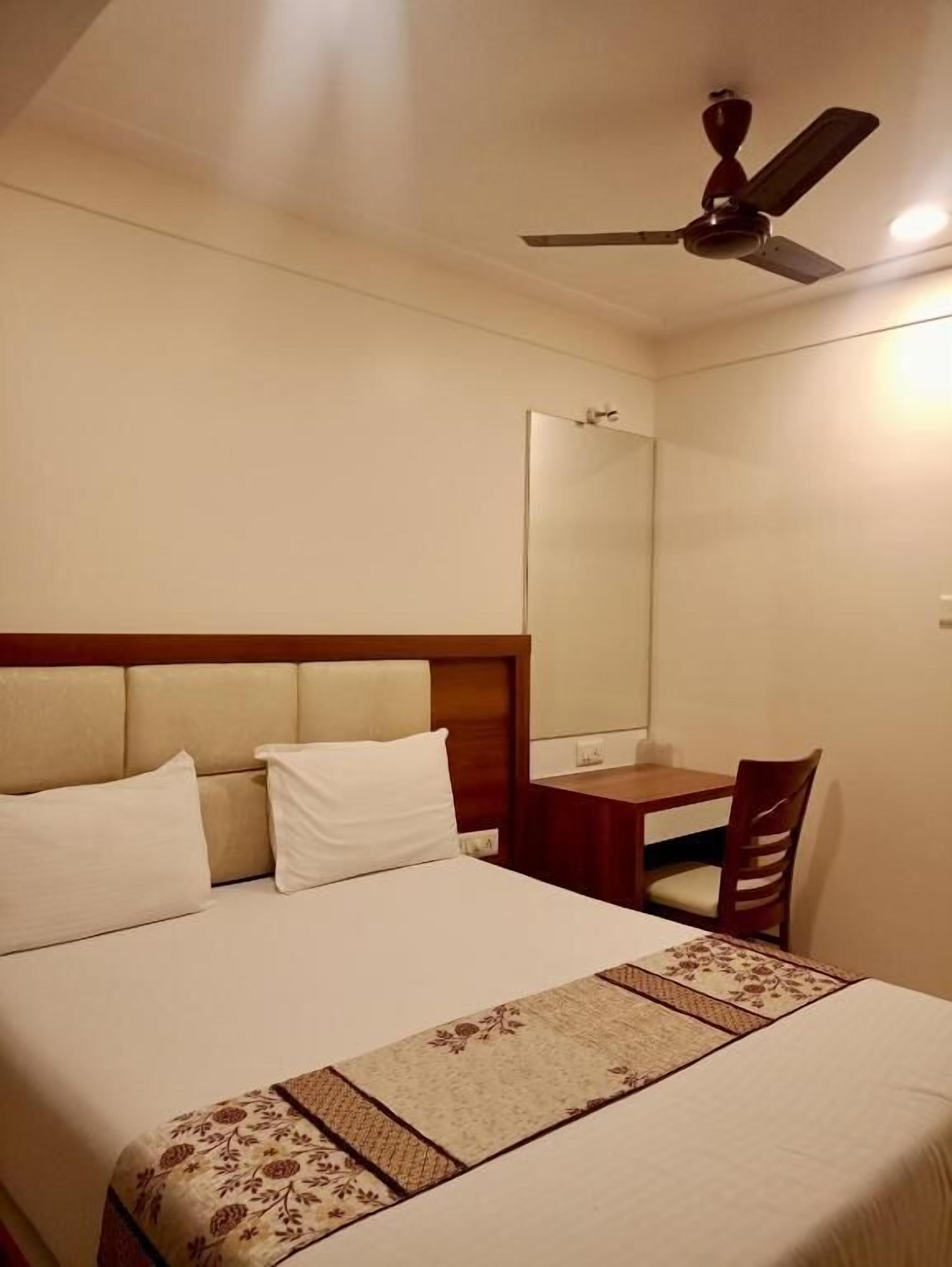 A hotel room with a bed, a desk, a chair, a ceiling fan, and a mirror.