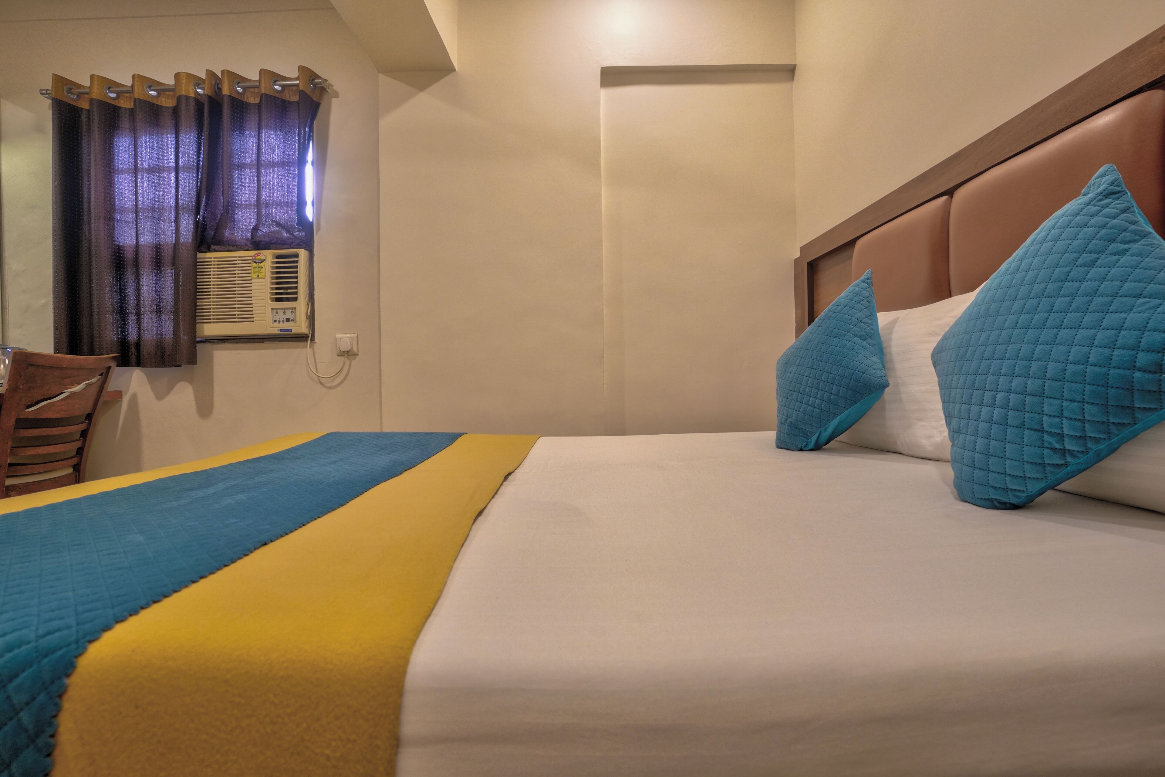 Une chambre d’hôtel équipée d’un lit, d’une chaise, d’une fenêtre avec des rideaux et d’un appareil de climatisation.
