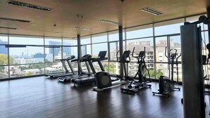Un gimnasio con cintas de correr, bicicletas estáticas y elípticas, con amplias ventanas que ofrecen vistas a la ciudad.