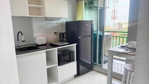 Una cocina moderna con armarios blancos, un refrigerador negro, horno empotrado y un pequeño comedor con una mesa y un taburete.