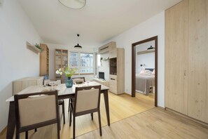 A modern, well-lit room with a dining table, chairs, and a kitchen area. - Comfortable Apartment | Balcony | Private Parking (Warszawa)