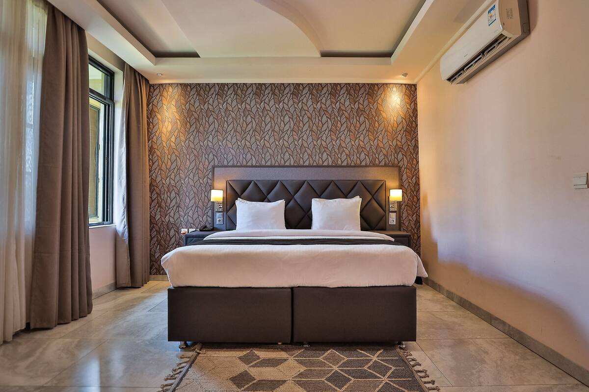Une chambre d’hôtel avec un grand lit, une tête de lit dotée de lampes, un mur décoré d’un motif et un appareil de climatisation.