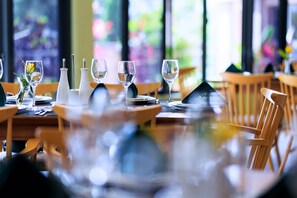 Una mesa de restaurante dispuesta con copas de vino, saleros y pimenteros, y un pequeño florero con una flor.